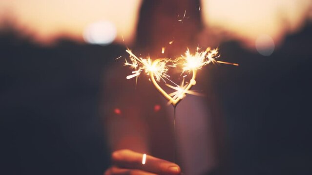 Hand of woman hold glow burn fireworks heart shape sparkler at sunset, love, valentine's day.