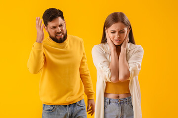 Fototapeta premium Young couple suffering from loud noise on yellow background