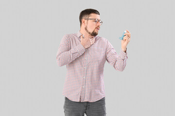 Sick man with inhaler on light background