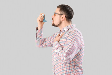 Sick man with inhaler on light background