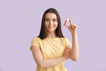 Young woman with bottle of vitamin supplements on lilac background