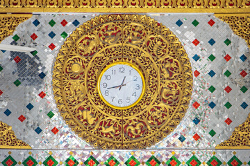 Golden clock on the decorative wall of a Buddhist temple, Thailand