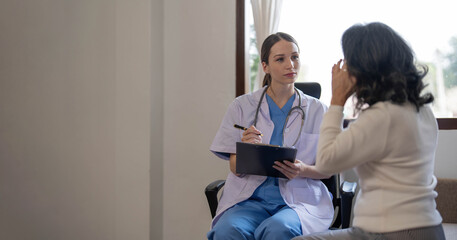 Asian female patient undergoing health check up while female doctor uses stethoscope to check heart...