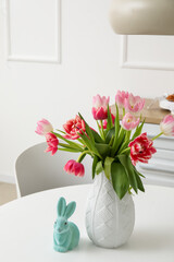 Vase with tulips and Easter rabbit on dining table in kitchen