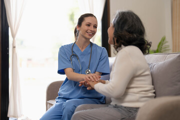 Happy patient is holding caregiver for a hand while spending time together. Elderly woman in nursing home and nurse.