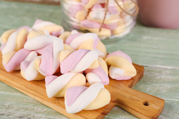 Board and jar of delicious twisted marshmallows on green wooden table