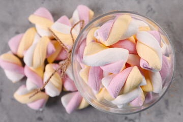 Jar and heap of delicious twisted marshmallows on grey table