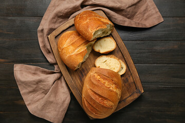 Cutting board with fresh sliced bread on black wooden background