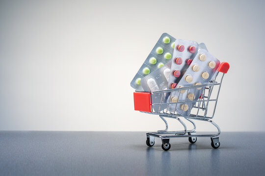 Shopping cart with different tablets and pills blister pack on grey background with copy space. Buy and shopping medicine concept.