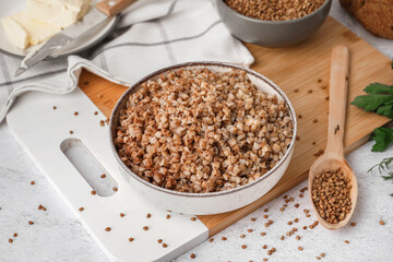 Board with bowl of tasty buckwheat porridge on white table