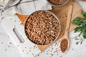 Board with bowl of tasty buckwheat porridge on white table