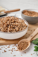 Board with bowl of tasty buckwheat porridge on white table