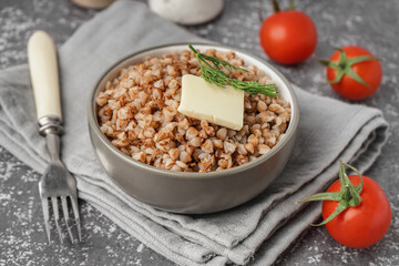 Bowl of tasty buckwheat porridge with butter, dill and fresh tomatoes on grey table