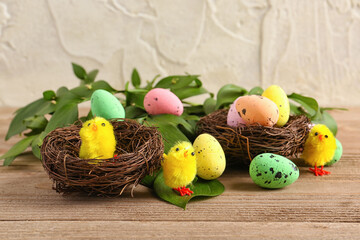 Nests with Easter eggs, toy chicks and plant leaves on wooden table