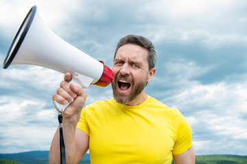 man in yellow shirt shout loud in loudspeaker on sky background