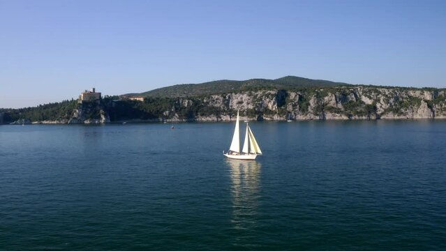 sailing boat in trieste gulf with hills and duino castle in background