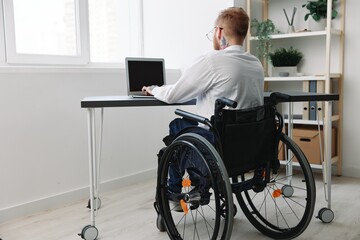 Fototapeta na wymiar A man wheelchair businessman with tattoos in the office works at a laptop online, business process, a wheelchair close-up, integration into society, the concept of working a person with disabilities