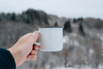 Close-up of caucasian male hand holding white enameled mug with an empty space for advertising on...