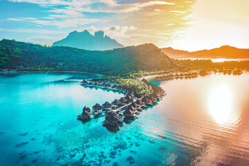 Luxury travel vacation aerial of overwater bungalows resort in coral reef lagoon ocean by beach. View from above at sunset of paradise getaway Bora Bora, French Polynesia, Tahiti, South Pacific Ocean - obrazy, fototapety, plakaty