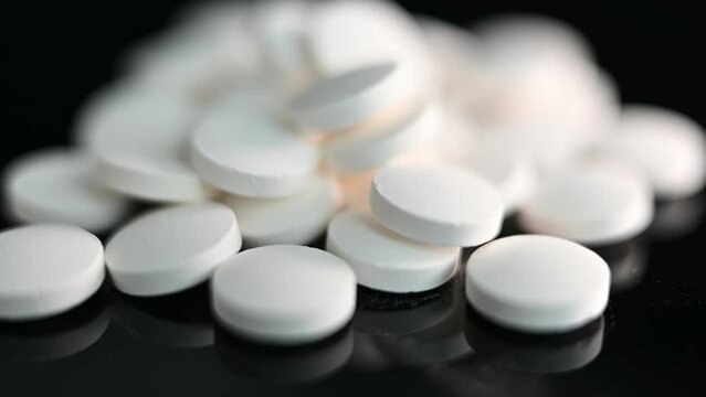 Close up of a pile of generic white pills in on a reflective surface