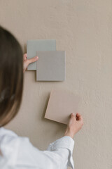 Hands of female designer pinning paper card mockups  to wall in studio. Mood board ideas template.