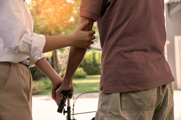 Young woman helping and supporting her elderly grandfather walking outdoor together in a home...
