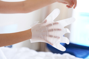 Obraz premium After a shower, a girl wrapped in a towel uses cosmetic gloves to moisturize the skin of her hands. Cosmetic trends for body care at home