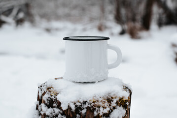 Iron enameled white mug mock-up standing on stump in snowy forest, close-up