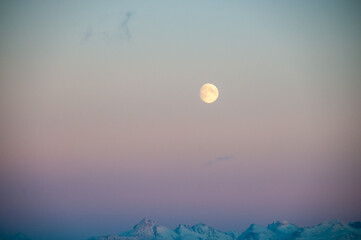 Fototapeta premium Landscape shot highlighting a near full moon over the rugged mountains of arctic Norway, near Bodo, during golden hour.