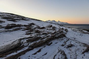 Landscape shot highlighting the rugged mountains and snow-covered beaches of arctic norway during a brief golden hour during the long winters.