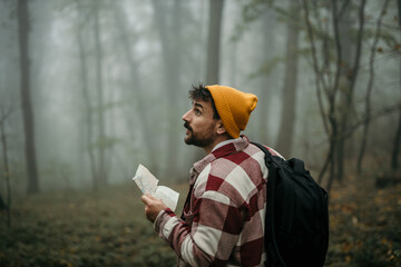 A male backpacker walking in the forest, holding a map and looking for the right path.