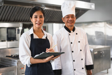 Asia woman assistant chef holding clipboard with senior chef and kitchen background	