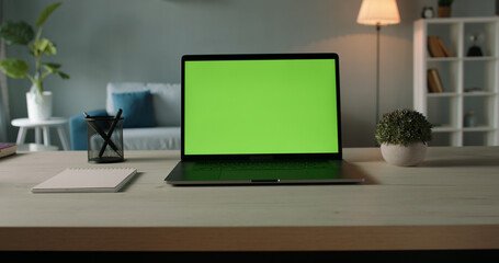 Modern laptop with mock up chroma key green screen on table of living room, desk set up for work at home - technology concept close up