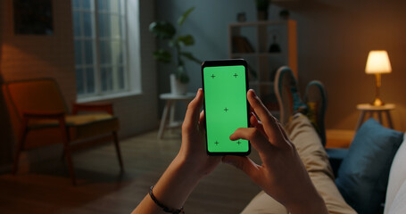 Man lying on couch using smartphone with chroma key green screen at night, scrdoing various gestures like swiping and scrolling - internet, communications concept close up 