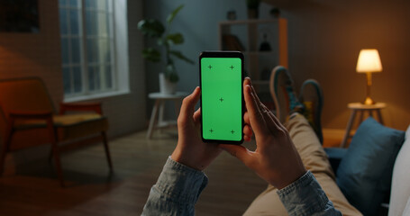 Close up shot of guy lying on couch at night, holding a smartphone with chroma key mock up green screen - technology, connections, communications concept