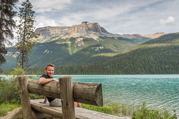 Fototapeta na wymiar Caucasian tourist smiling on a wooden bench at the shore of Emerald lake in Yoho National park, British Columbia, Canada