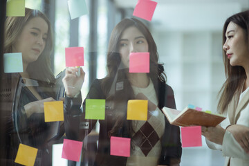 Team of asian business woman working with paper note on glass wall, Business people meeting to share idea at office, Business planning and Sticky note on glass wall.