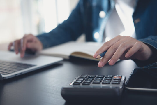 Business woman calculating monthly expenses, managing budget. Woman sitting at table using calculator to calculate tax refund, working at office with laptop computer on table, close up