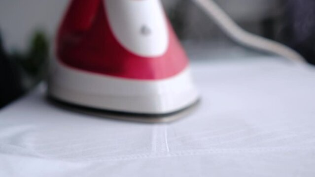 Selective focus of female hand irons white clothes with steam iron on an Ironing board.  Ironing linen using hot steam. Push button of steam humidifier, laundry moistening function. Housework concept