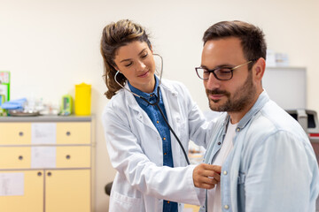 Caring Caucasian female doctor use phonendoscope examine male patient heart rate at consultation in...