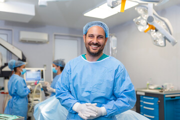 Portrait of male nurse surgeon or staff member dressed in surgical scrubs gown mask and hair net in hospital operating room theater making eye contact smiling pleased happy looking at camera