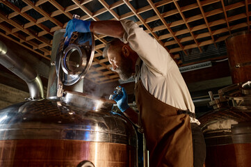 Handsome adult brewer inspecting process of brewing beer with steam