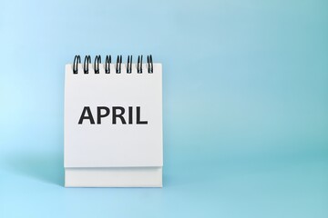 Selective focus of April desk calendar on blue background with spring leaves and copy space. 