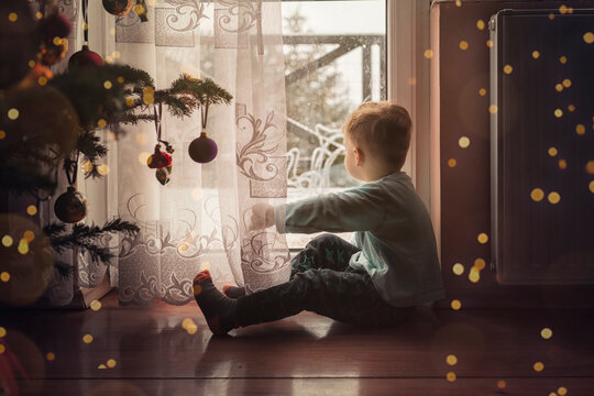 Toddler boy sitting on the floor by the window next to a christm