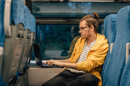 Young teenage man with glasses travels in train with laptop.