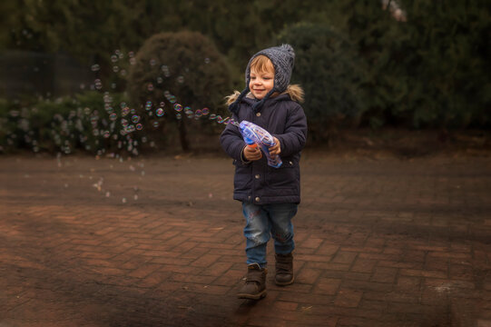 Toddler in warm clothes playing with bubble gun outside