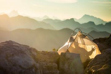 Man reaches out from tent, touching nature, mountains.