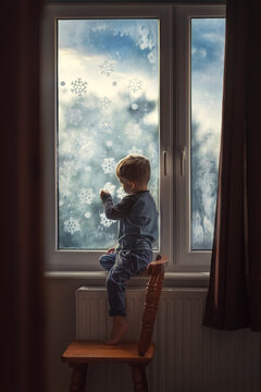 Small boy in blue clothes sitting on window sill and attaching c
