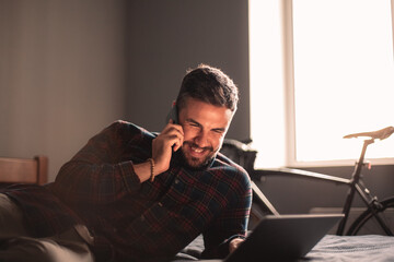 Happy businessman talking on smart phone using laptop computer at home