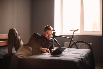 Happy man using laptop computer on bed at home